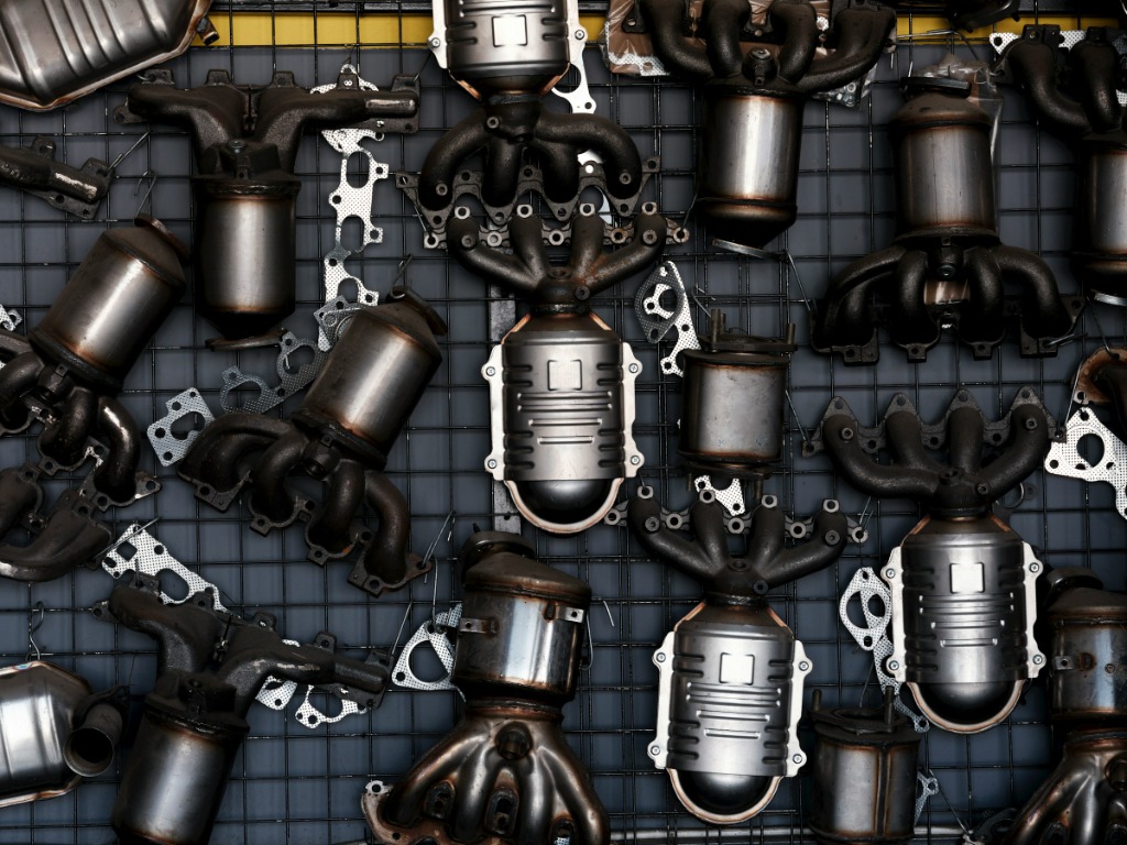 Assortment of aftermarket exhaust manifolds and catalytic converters displayed on a wire grid